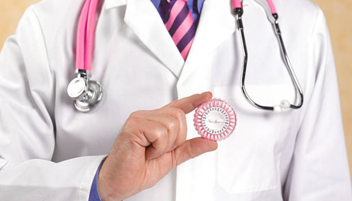 A man in a white coat holding a pink condom, promoting safe sex